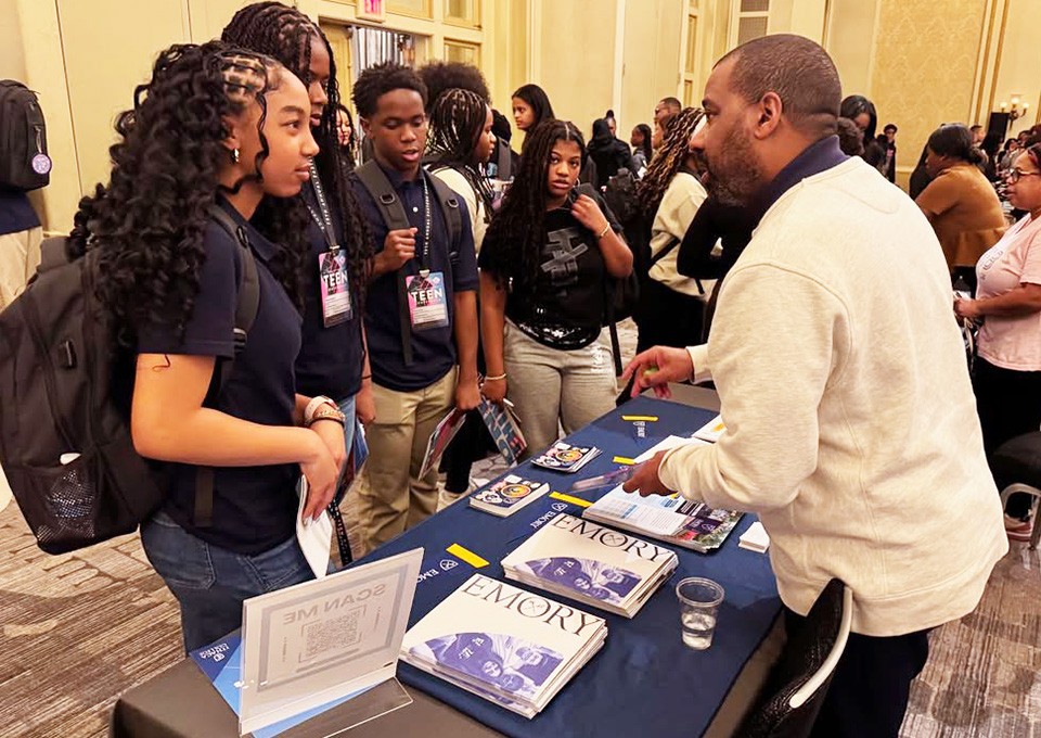high school students talk to Emory admissions officer at a college fair